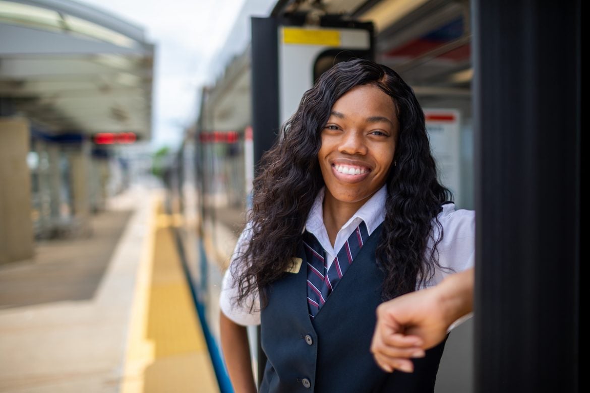 Headshot of MetroLink operator, Shatifa Hudson, leaning in the doorway of a MetroLink train. The train is stopped at a station and the platform appears on the left.